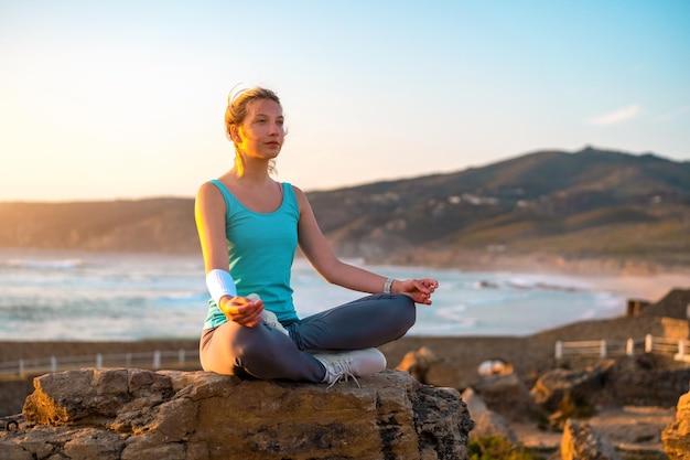 Woman practice yoga lotus pose to meditation with summer vacation rocky beach happiness and relaxation Calm female exercise with yoga meditate ocean beach with sunset golden time