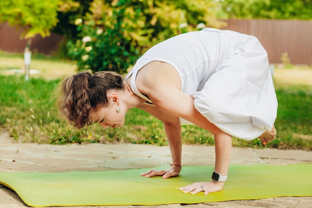 Woman practices yoga in summer garden Kakasana Crow Pose with bent arms