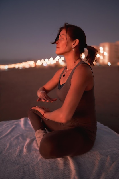 Woman practicing reiki or meditation on the beach in the city at sunset