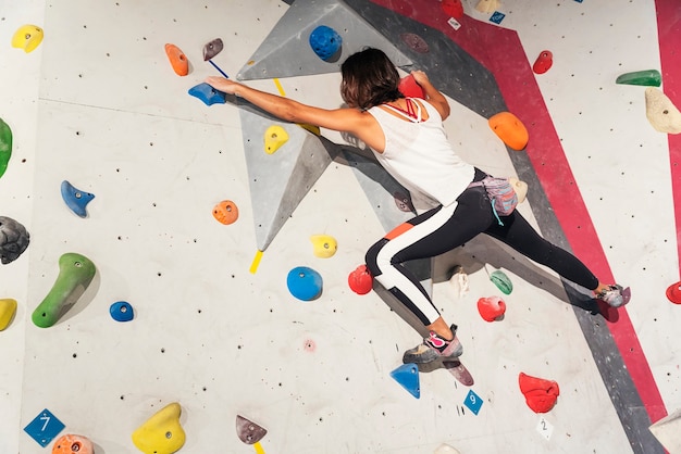 Woman practicing rock climbing on artificial wall indoors. Active lifestyle and bouldering concept.