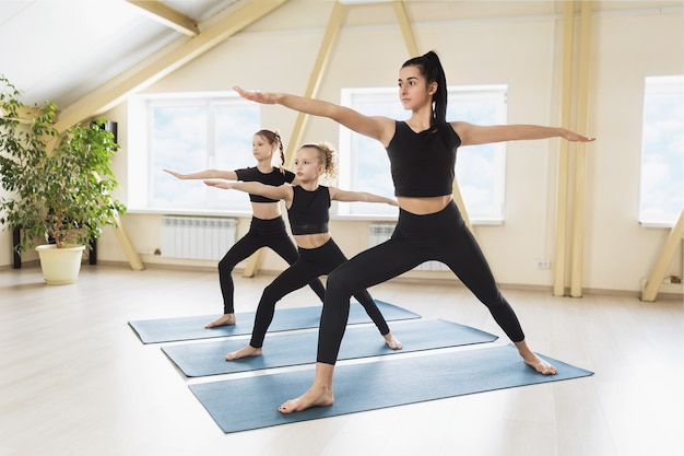 Woman practicing yoga conducting a training session with two students showing the correct execution of Virabhadrasana exercise warrior pose