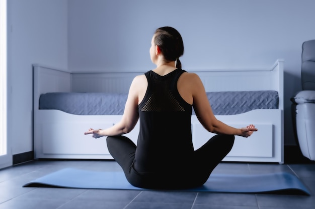 Woman practicing yoga indoor for training stretching and relaxation lotus posture on carpet