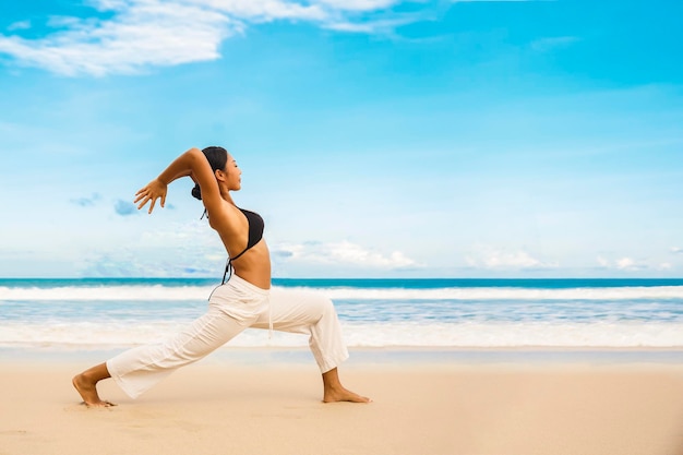 Woman practicing yoga at seashore of tropic beachSports lady standing at the beach make yoga exercises