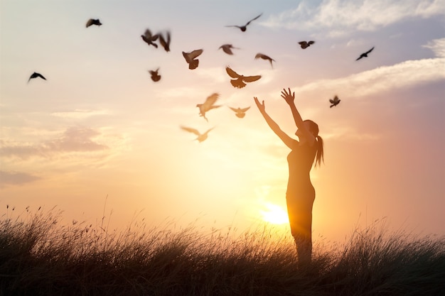 Woman praying and free the birds to nature on sunset background