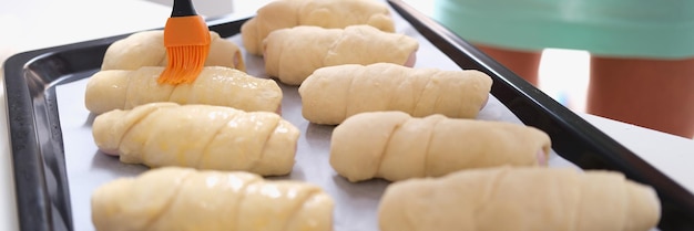 Woman prepares croissants and brush dough with egg yolk