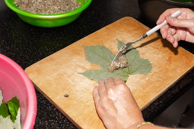 A woman prepares food at home Minced meat is placed in grape leaves on a wooden board cooking dolma