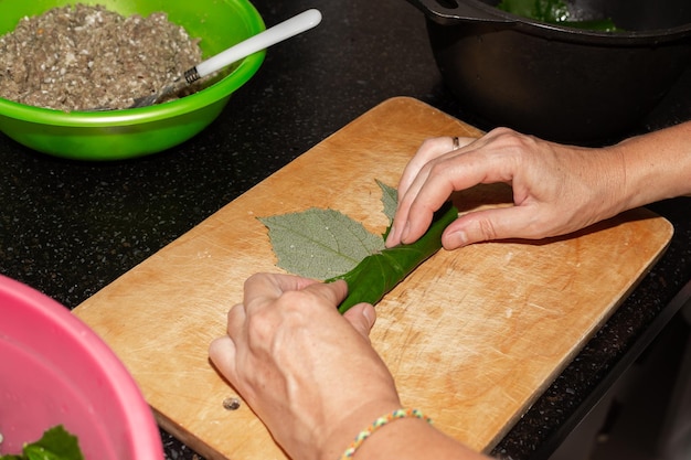 A woman prepares food at home Minced meat is wrapped in grape leaves on a wooden board dolma