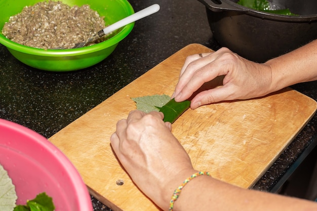 A woman prepares food at home Minced meat is wrapped in grape leaves on a wooden board dolma