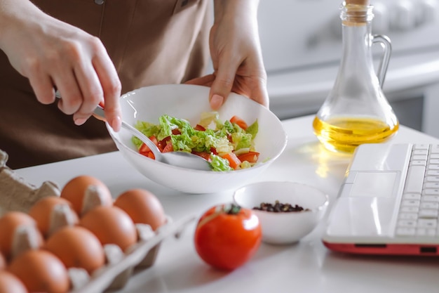 Woman preparing diet salad using digital cookbook Fresh vegetables and laptop in home kitchen