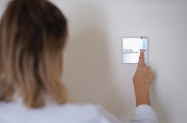 Woman pressing button on remote control of air conditioner in wall closeup