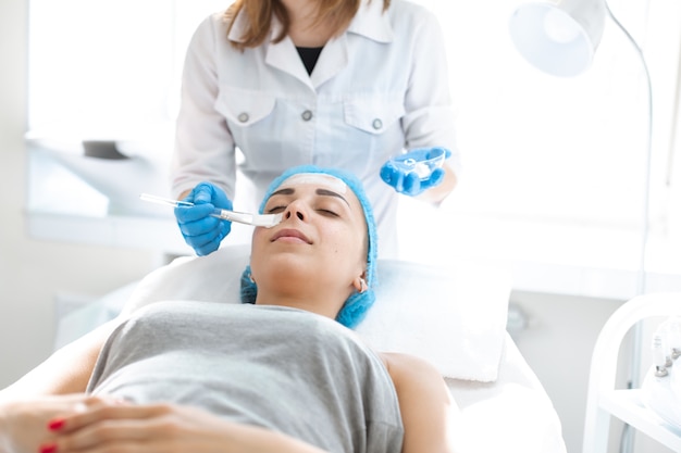 Woman professional doctor beautician applies a mask on patients face for skin care