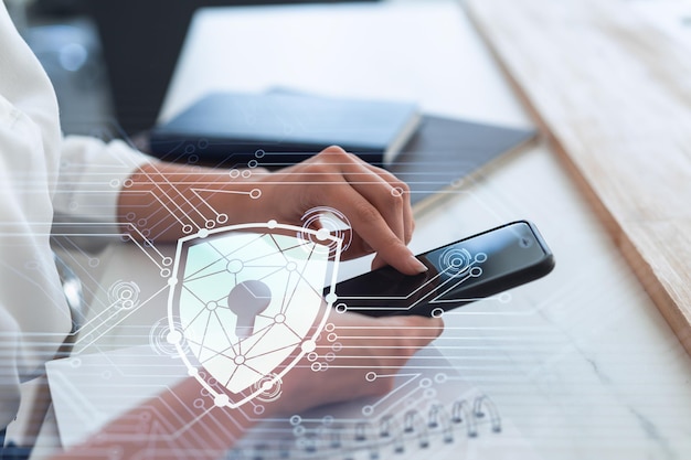 A woman programmer is browsing the Internet in smart phone to protect a cyber security from hacker attacks and save clients confidential data Padlock Hologram icons over the typing hands Formal wear