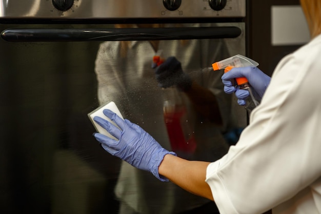 Woman in protective gloves cleaning the oven door