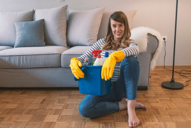 Woman in protective gloves is holding a bucket with things for cleaning 