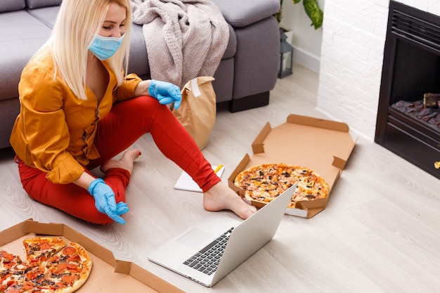 Photo woman in protective gloves and mask with pizza at home during quarantine. service food order online delivery in quarantine covid-19. airline food.