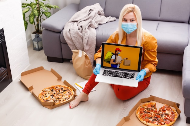 Photo woman in protective gloves and mask with pizza at home during quarantine. service food order online delivery in quarantine covid-19. airline food.