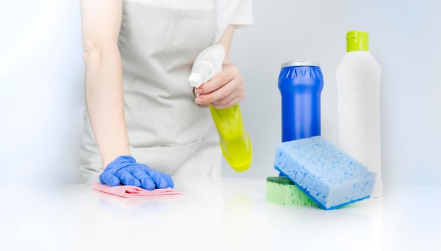 Woman in protective gloves and wiping dust using a spray and a duster while cleaning her house closeup