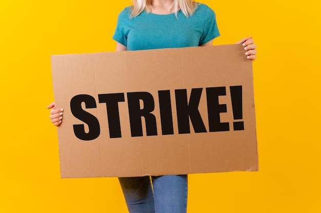 Photo a woman protesting holding a sign with the slogan of the hollywood actors and writers strike on a yellow background