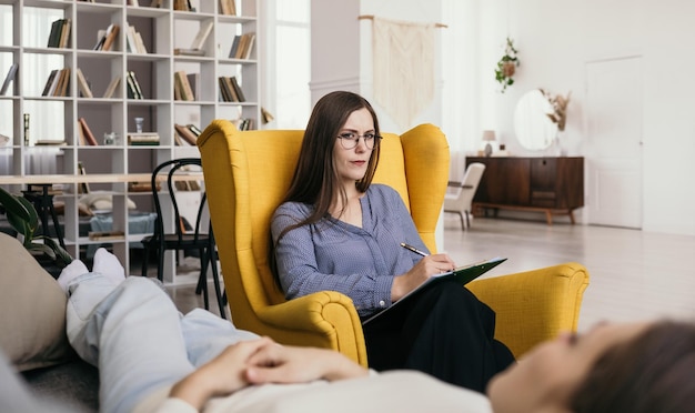 Photo a woman psychologist with glasses is sitting in an armchair and is consulting a patient on the couch. professional psychological assistance