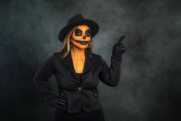 Woman in pumpkin makeup to celebrate Halloween pointing to a blank space.