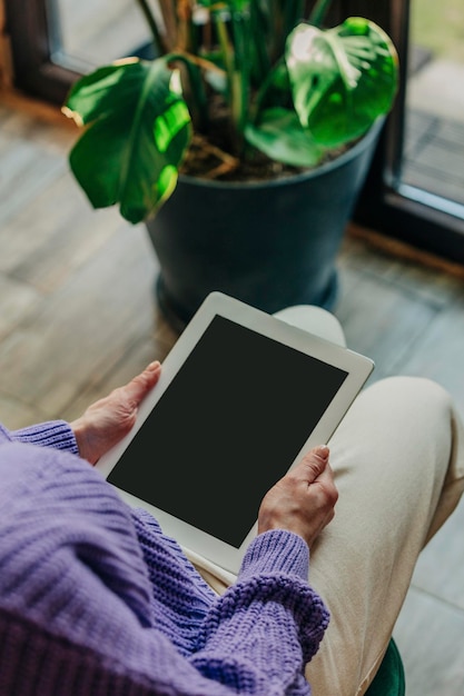 Woman in purple sweater sits in chair next to palm tree and using tablet