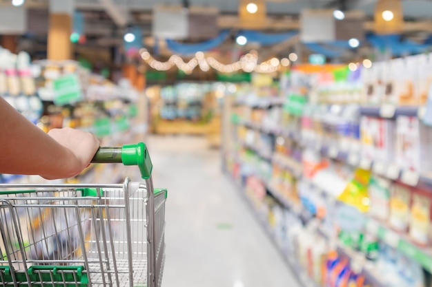 Woman pushing shopping cart with blur supermarket aisle background