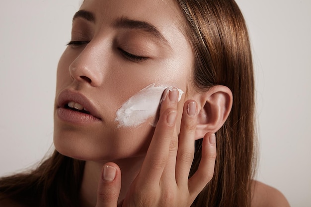 Woman put cream on a cheek ideal young skin concept