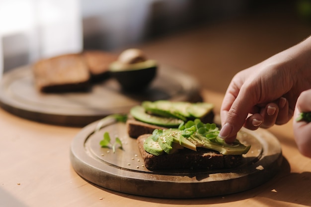 Woman put mustard seedlings on avocado sandwich with dark rye toasted bread made with fresh sliced