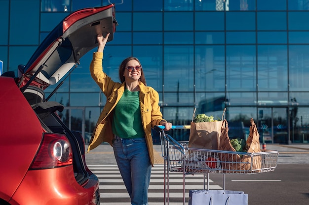 Woman put shopping paper bags with a groceries in cars trunk