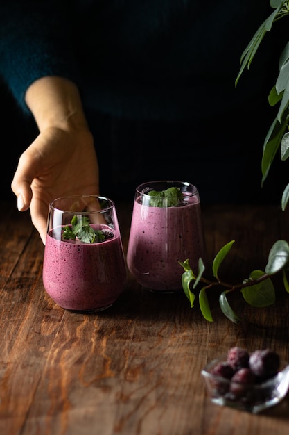 Photo a woman puts a berry smoothie with greens on the table