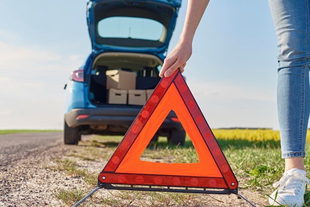 Woman puts an emergency stop sign near broken car on the road