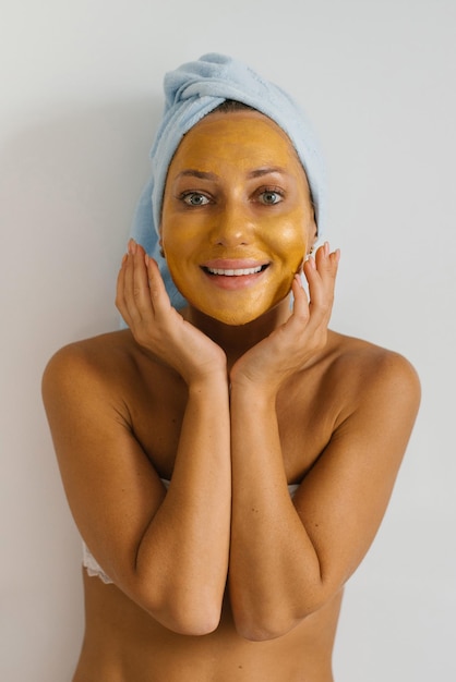 Woman puts a golden mask on her face smiling Home bright bathroom Natural skin care