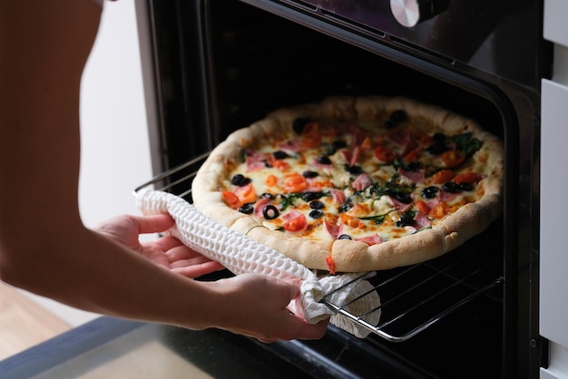 Photo woman puts pizza pan in oven closeup