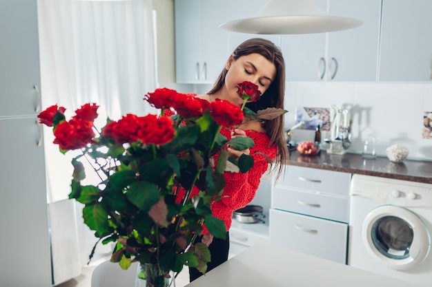 Woman puts roses in vase smelling flower housewife taking care of coziness on kitchen modern kitchen