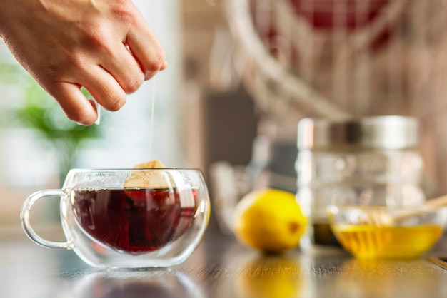 Woman puts the tea bag in the glass cup with hot water