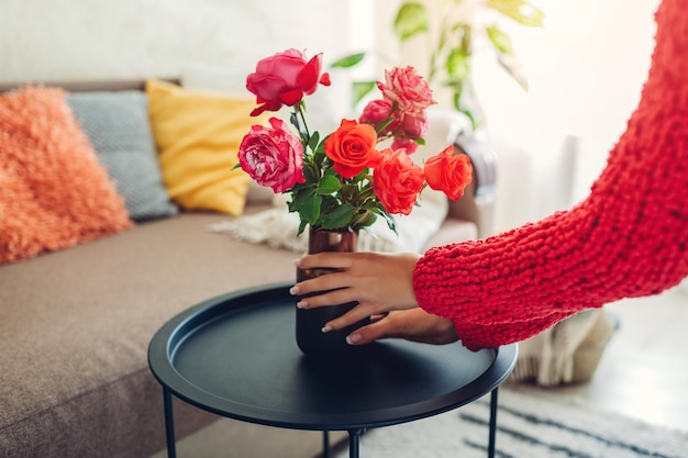 Woman puts vase with flowers roses on coffee table housewife taking care of coziness in apartment in