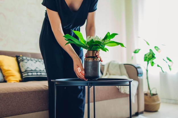 Woman puts vase with flowers on table Housewife taking care of coziness in apartment Interior and decor