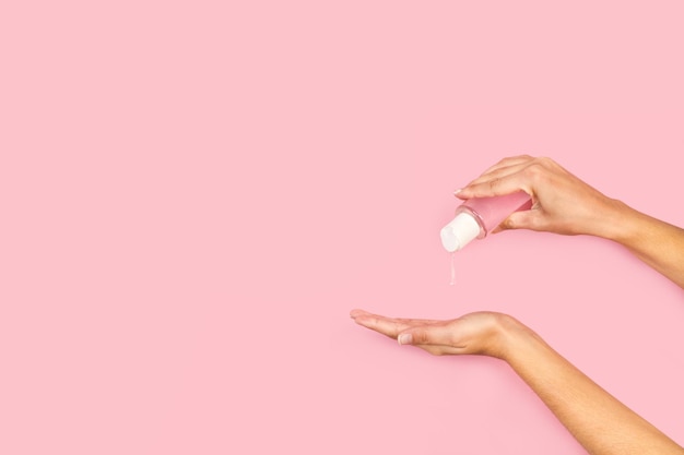 Woman putting alcohol gel on her  hand on a pink background with copy space