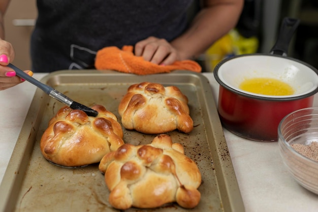 Woman putting butter on a pan de muerto that she finished baking at home