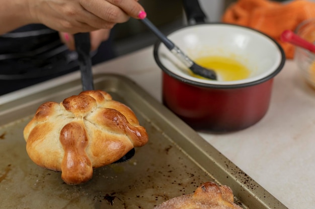 Woman putting butter on a pan de muerto that she finished baking at home