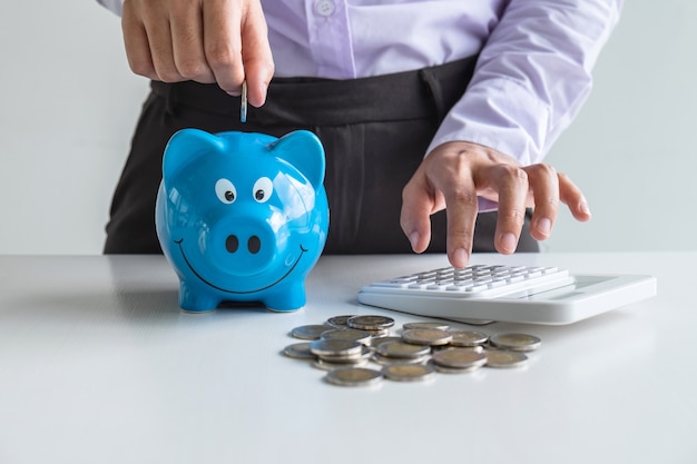 Woman putting coin in blue piggy bank for step up growing business to profit and saving with piggy bank, Saving money for future plan and retirement fund concept.