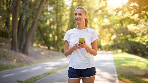 Woman putting on earphones to listen music before jogging summer park