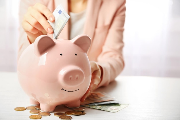 Woman putting euro banknote into a piggy bank on the table Financial savings concept