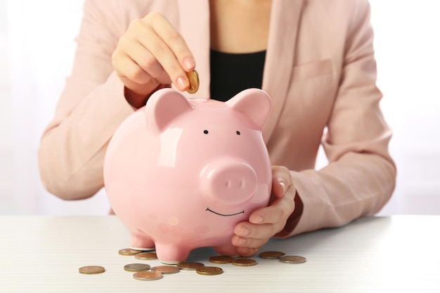 Woman putting euro coin into a piggy bank on the table Financial savings concept