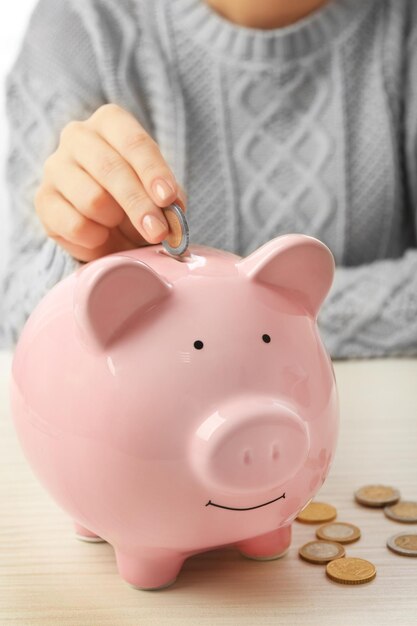 Woman putting euro coin into a piggy bank on the table Financial savings concept