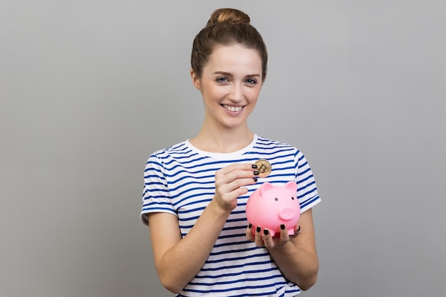 Woman putting physical bitcoin into piggy bank investment in cryptocurrency concept