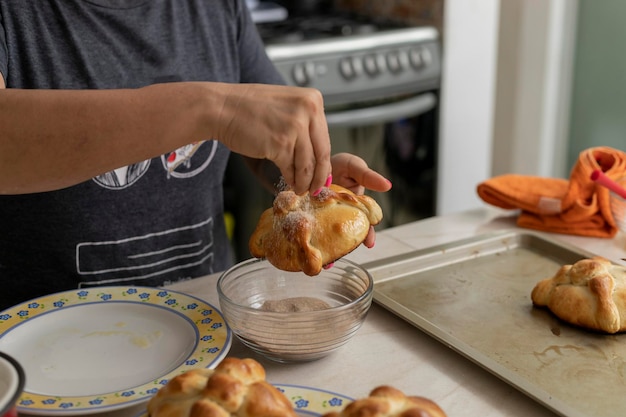 Woman putting sugar on a freshly baked bread of the dead at home