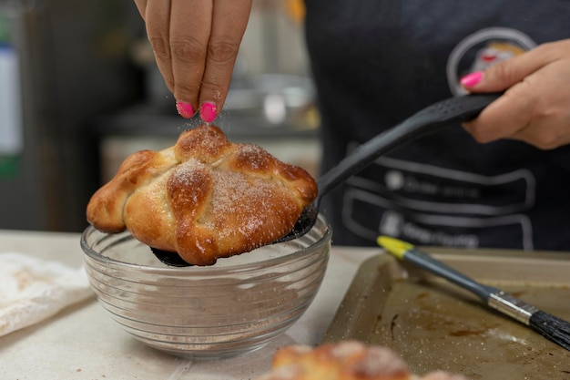 Woman putting sugar on a freshly baked bread of the dead at home