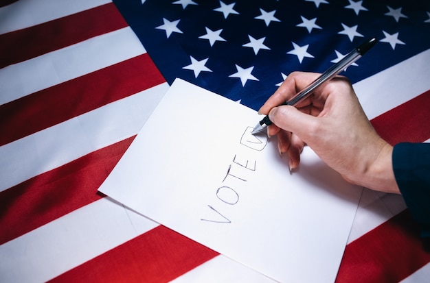 Woman putting tick on the paper for vote. Political changes in the country. Copy space place. Elections in the USA. American flag. People voting on ballot.