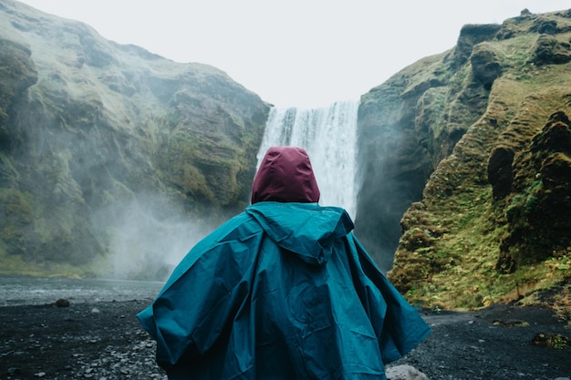 Woman on rain clothes in front of Skogafoss waterfall in Iceland during a moody day Travel on van concept road trip style Visit Iceland and north countries conceptCopy space image